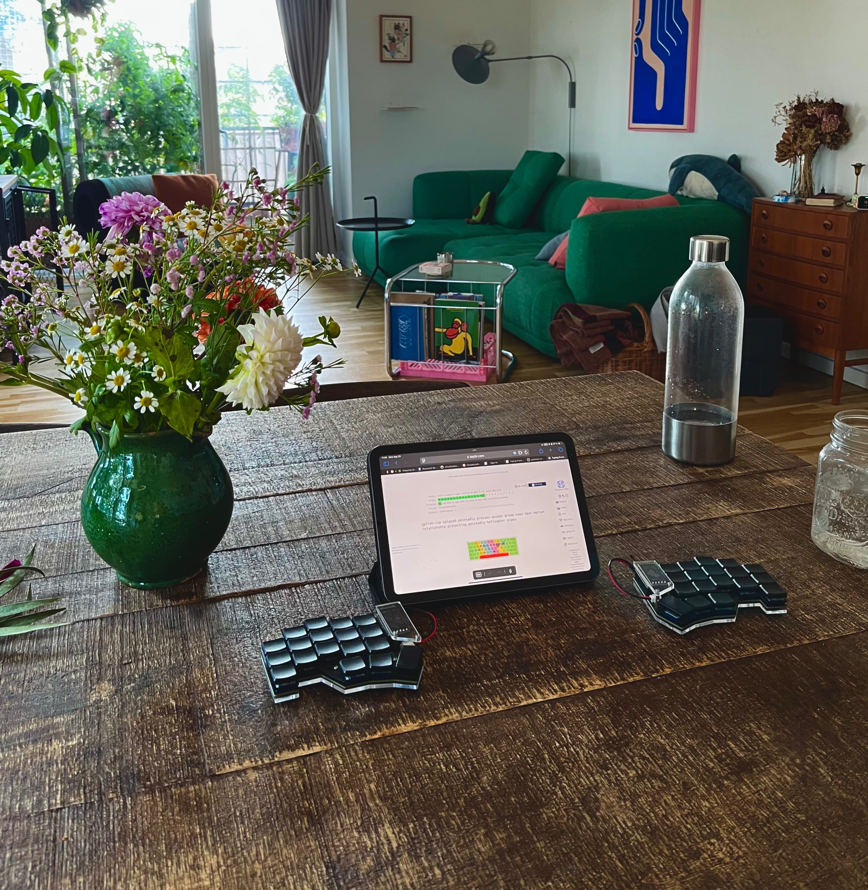 a split keyboard on a table with an ipad. There is a bunch of colorful furniture in the background